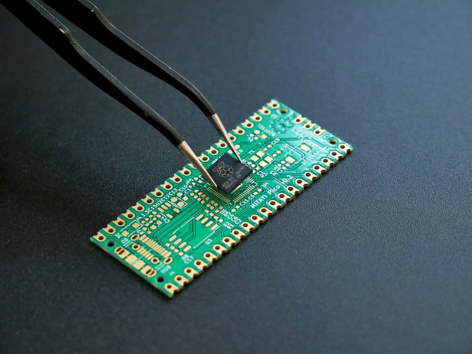 Engineer holding a microcontroller with tweezers above a green circuit board